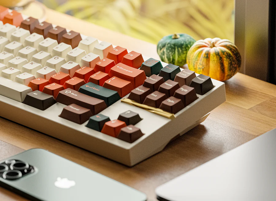 A fall color coated keyboard with two small pumpkins sitting near by. 