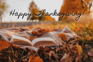 A book open on a field in autumn with the words Happy Thanksgiving!
