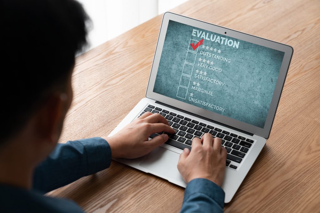 A view looking over someone's shoulder as they work on a laptop computer. The screen is titled Evaluation and there are options for a survey below.