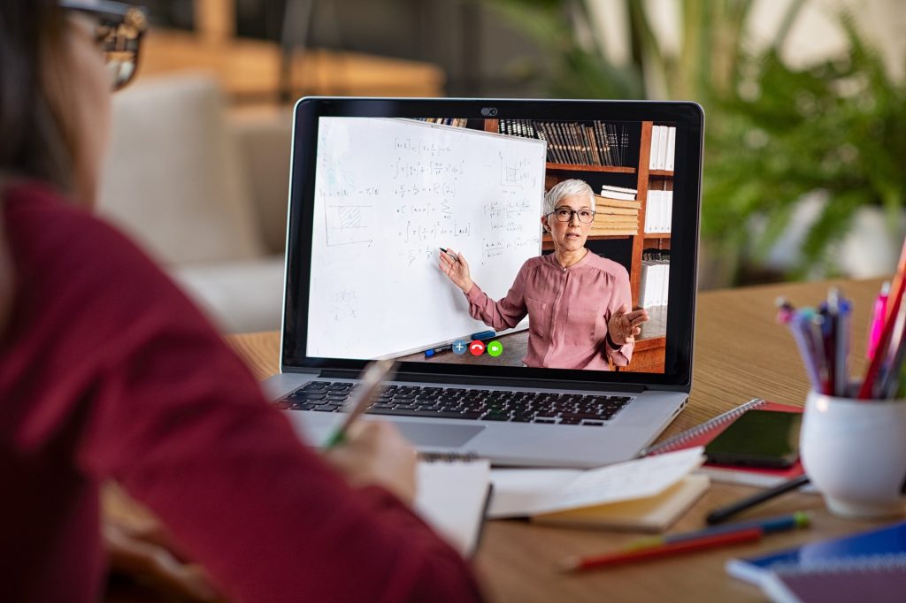 A person looking at a computer that shows a woman teaching an online course