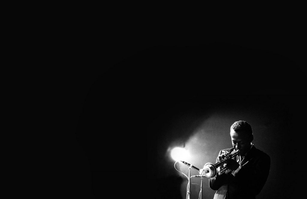 Jazz trumpeter Miles Davis in a spotlight with a black background.